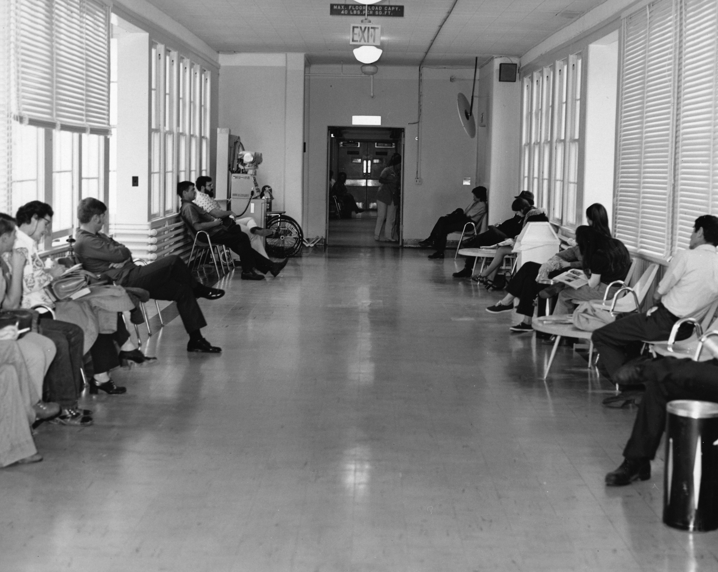 A crowded hospital waiting room with patients seated on both sides of a long hallway
